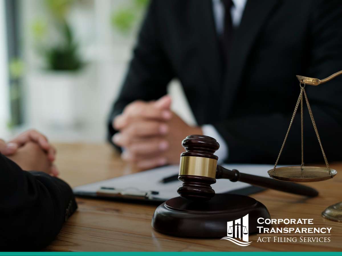 A lawyer consulting with a client in an office, scales of justice and gavel on the table, logo for Corporate Transparency Act Filing Services visible